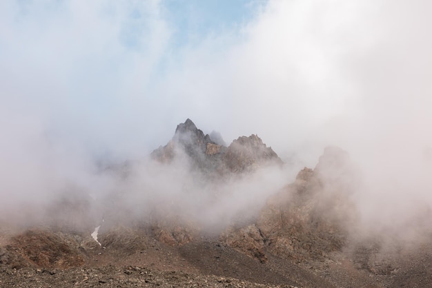 Scenic alpine landscape with rocky mountains in dense low clouds in morning sunlight Colorful mountain scenery with sharp rocks among thick low clouds Awesome view to high rockies in low cloudiness