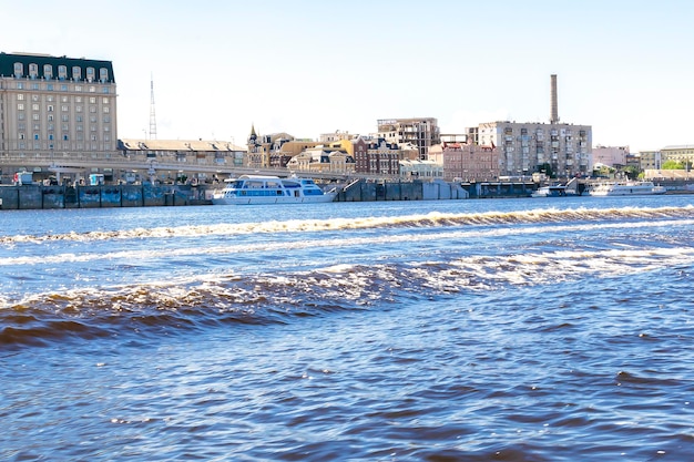 푸른 물 다리 유람선이 있는 키예프의 드니프로 강(Dnipro river)의 아름다운 여행 도시 풍경은 화창한 여름날 강 항구에 있는 주거용 건물을 배송합니다.
