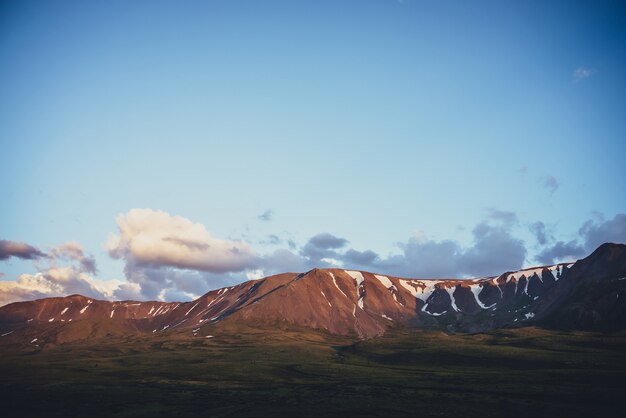 Scenic landscape with illuminating sunset clouds above mountains with snow.