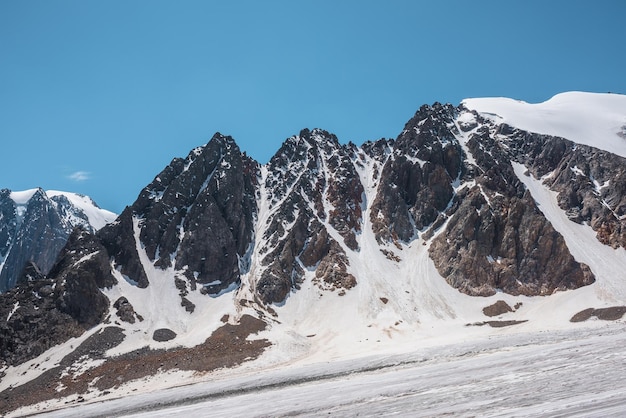 Scenic mountain landscape with glacier under sharp rocks in sunlight Awesome alpine landscape with glacial tongue in sunshine Beautiful view to snow mountain tops at very high altitude in sunny day