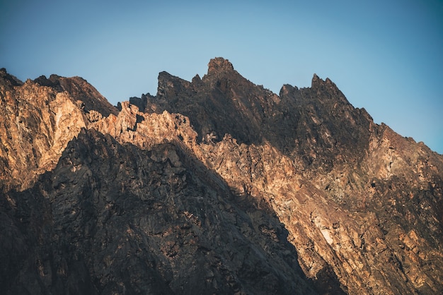 Scenic mountain landscape with great rocks in golden sunlight. Awesome rocky wall with sharp top in gold sunshine. Colorful sunny scenery with high rocky mountain with pointed pinnacle. Mountain wall.