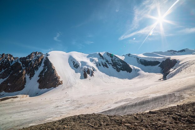 写真 日光の下で大きな氷河のある風光明媚な山の風景青い空の太陽の下で氷河の舌を持つ素晴らしい風景晴れた日の非常に高い標高にある雪の山の頂上への美しいアルプスの景色