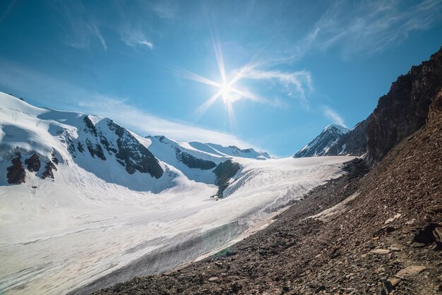 Scenic mountain landscape with large glacier in sunlight Awesome scenery with glacial tongue under sun in blue sky Beautiful alpine view to snow mountain tops at very high altitude in sunny day