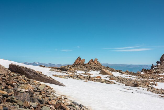 Scenic mountain landscape with old rocks and stones among snow in sunlight awesome alpine scenery with stone outliers on high mountain under blue sky in sunny day sharp rocks at very high altitude