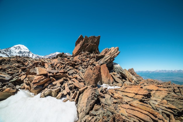 Scenic mountain landscape with old rocks and stones among snow in sunlight Awesome alpine scenery with stone outliers on high mountain under blue sky in sunny day Sharp rocks at very high altitude