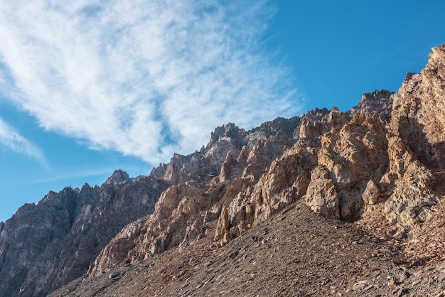 Scenic mountain landscape with sharp rocks under cirrus clouds in sunny day Colorful scenery with gold sunlit sharp rocky mountains High rocky mountains in golden sunlight under spindrift clouds