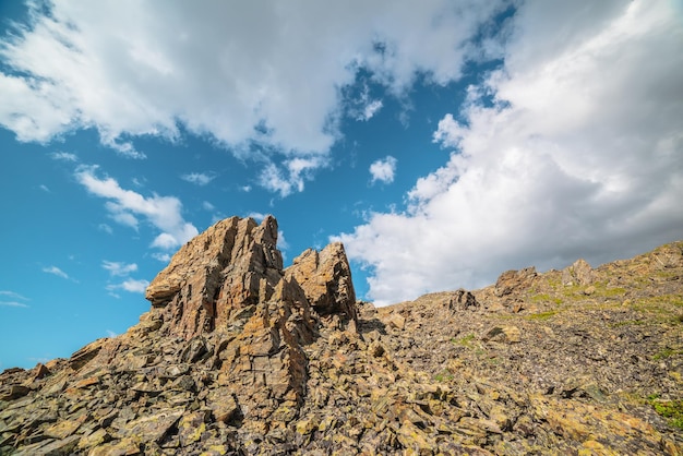 Scenic mountain landscape with stone outliers on rocky hill in sunlight under cloudy sky Colorful scenery with sunlit sharp rocks on stone mountain under clouds in blue sky at changeable weather