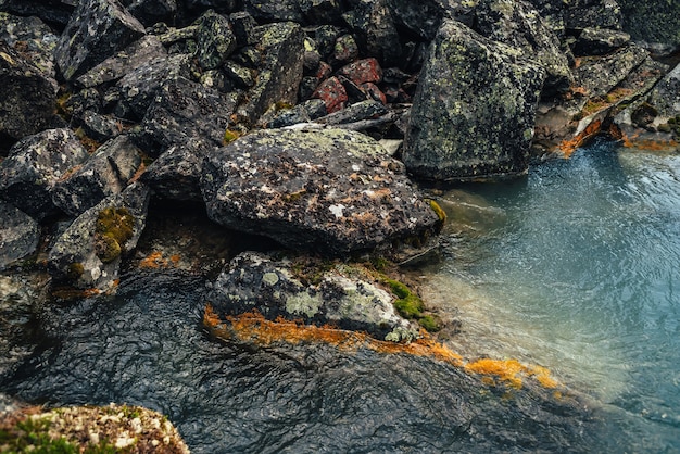 Scenic nature background of turquoise clear water stream among rocks with mosses and lichens. Atmospheric mountain landscape with mossy stones in transparent mountain creek. Beautiful mountain stream.