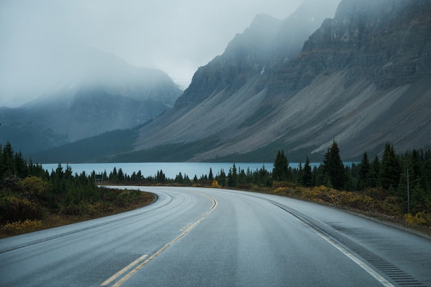 Photo scenic road trip with rocky mountain and lake in gloomy day