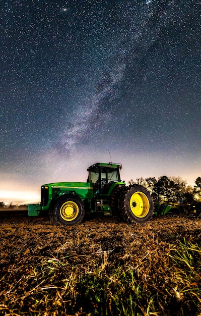 Scenic shot of a john deere green tractor in the middle of the\
agricultural field during the night