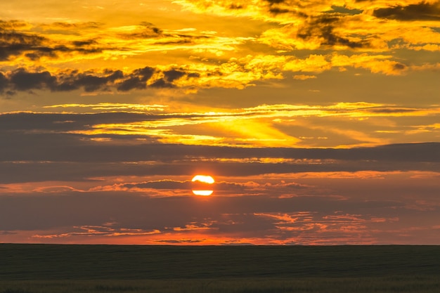 フィールドの暗いストリップに沈む夕日の風光明媚な空_