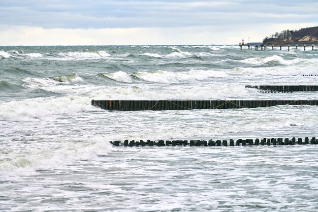 泡立つ波と青い海の風光明媚なビュー。海、冬のバルト海の風景にまで伸びるヴィンテージの長い木製の防波堤。沈黙、孤独、落ち着きと平和。