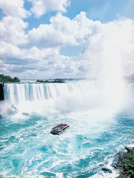 Photo scenic view of boat by waterfall against cloudy sky