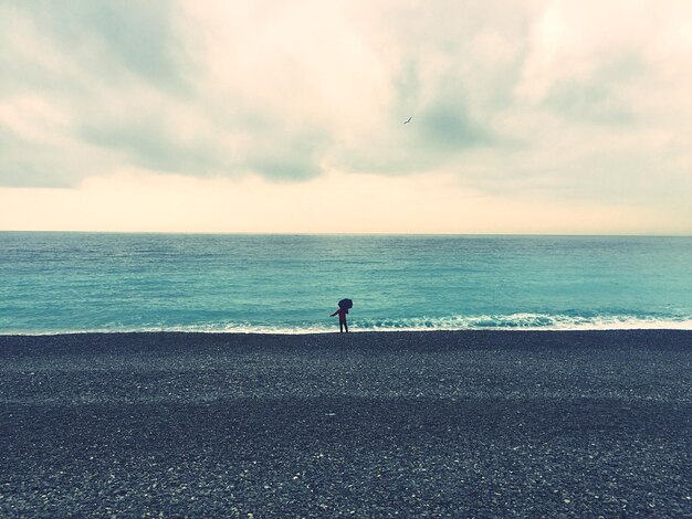 Foto vista panoramica di un bambino sulla spiaggia contro un cielo nuvoloso