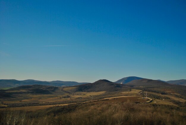 Scenic view of field and mountains against clear blue sky