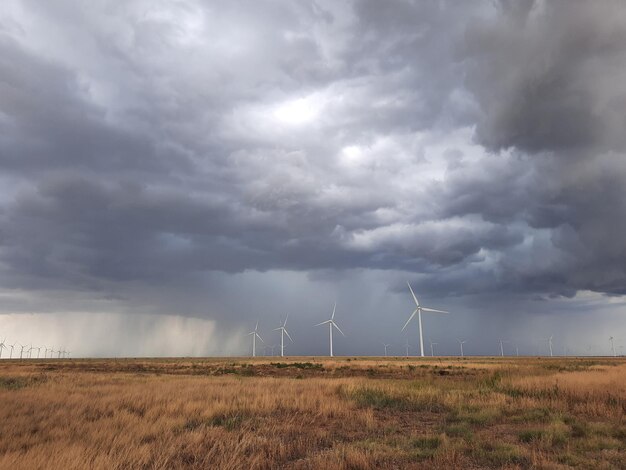 Photo scenic view of field with windmills against cloudy sky