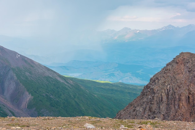 Vista panoramica dal bordo dell'abisso alle verdi colline e alla catena montuosa illuminata dal sole tra le nuvole piovose durante la pioggia paesaggio drammatico vicino al precipizio con la vastità della montagna alla luce del sole tra le nuvole con tempo variabile