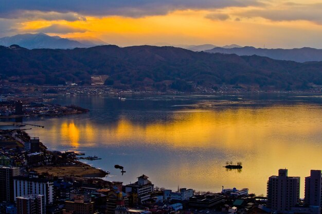 Scenic view of lake by buildings against sky during sunset