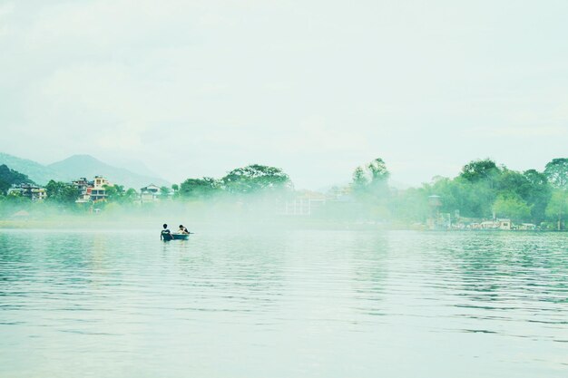 Scenic view of lake by trees in foggy weather