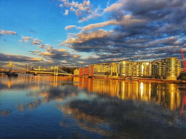 Scenic view of river by buildings against sky at sunset