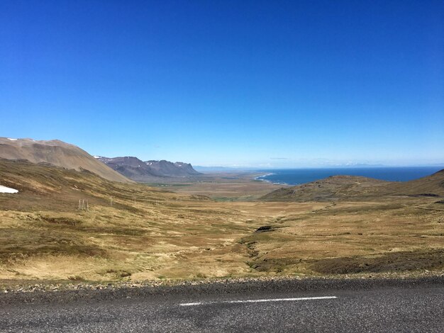 Scenic view of road by mountains against clear blue sky