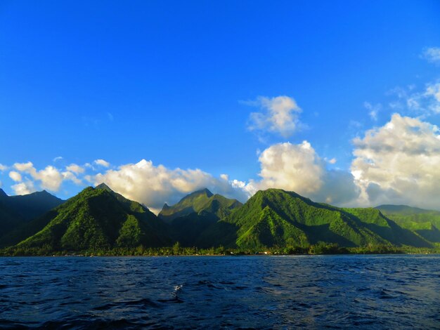 Scenic view of sea by mountains against blue sky