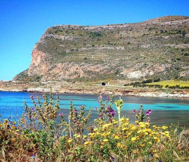 Scenic view of sea by mountains against clear blue sky