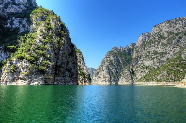 Scenic view of sea by mountains against clear blue sky