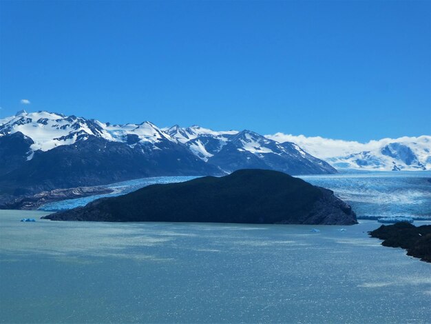 Scenic view of sea and snowcapped mountains against blue sky