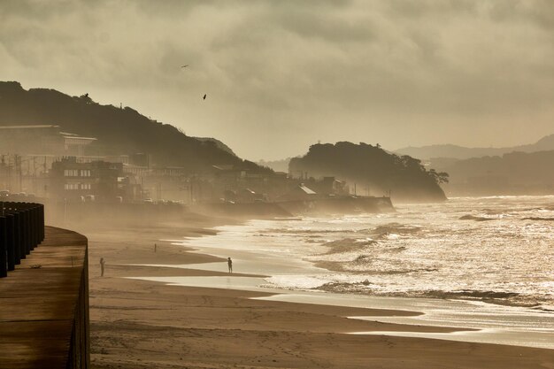 Scenic view of sea with silhouette people against moody sky during sunrise