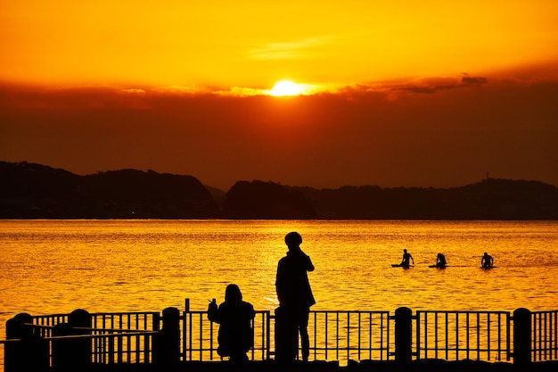 Scenic view of sea with silhouette people against orange sky during sunrise