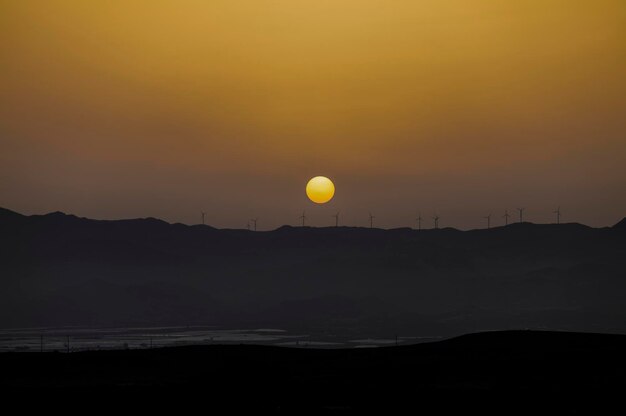 Photo scenic view of silhouette mountain with modern windmills against sky during sunset