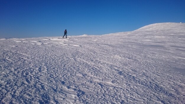 Scenic view of skiing uphills on snowcapped landscape against clear blue sky