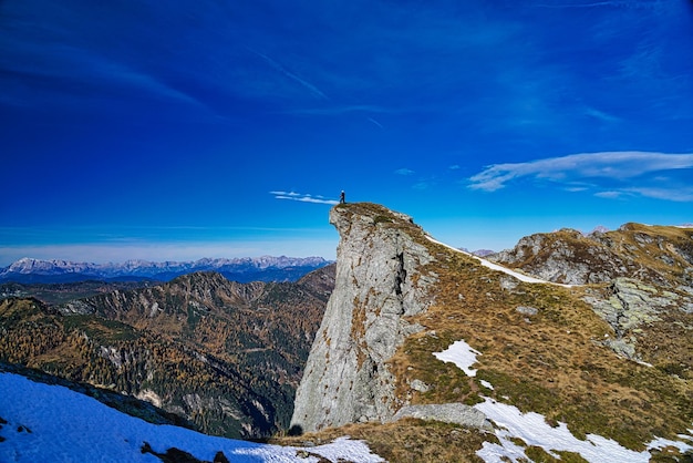 Foto vista panoramica delle montagne innevate contro il cielo blu con una persona sul punto più alto