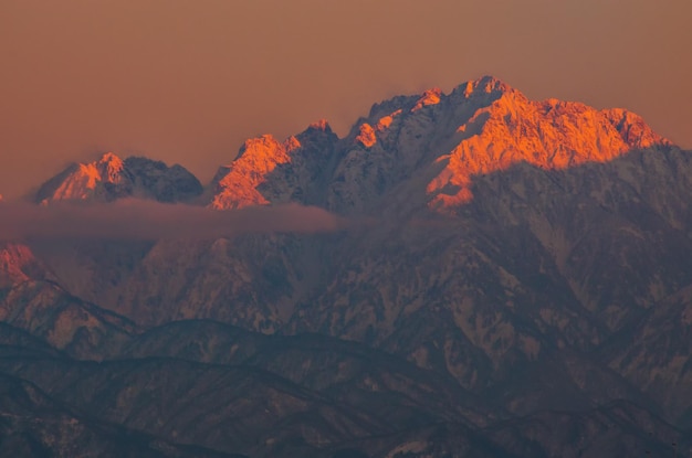 Photo scenic view of snowcapped mountains against orange sky