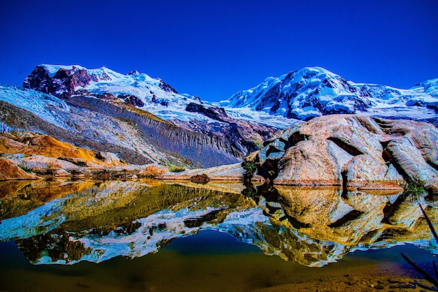 Foto la vista panoramica delle montagne innevate e il suo riflesso nel lago contro un cielo blu limpido