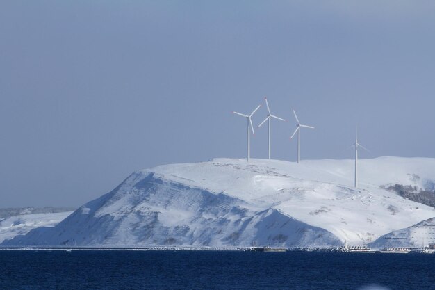 空の背景に風力タービンがある雪に覆われた山の景色
