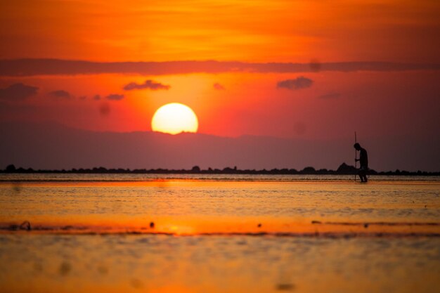 Scenic view of sunset over sea with silhouette man standing with stick against sky