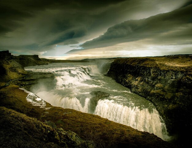 Photo scenic view of waterfall against cloudy sky