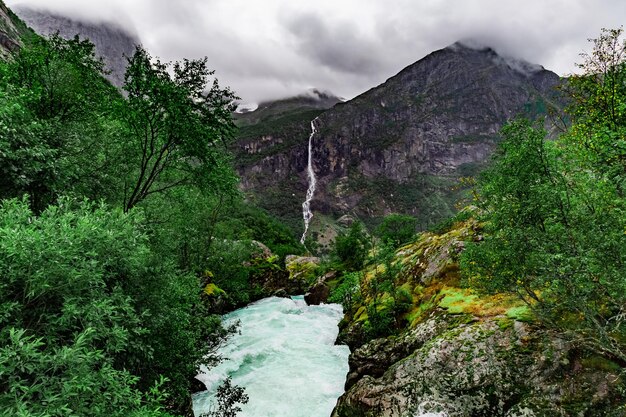 Photo scenic view on waterfall river and norwegian mountains against cloudy dramatic sky