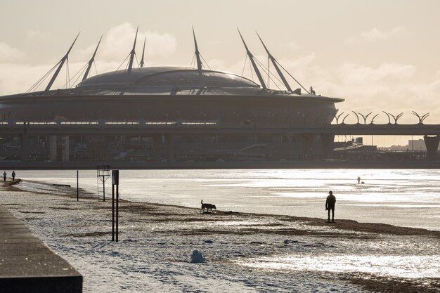 Scenic winter sea coast  of the 300 Years Park and a huge stadium with man figure walking with the dog.