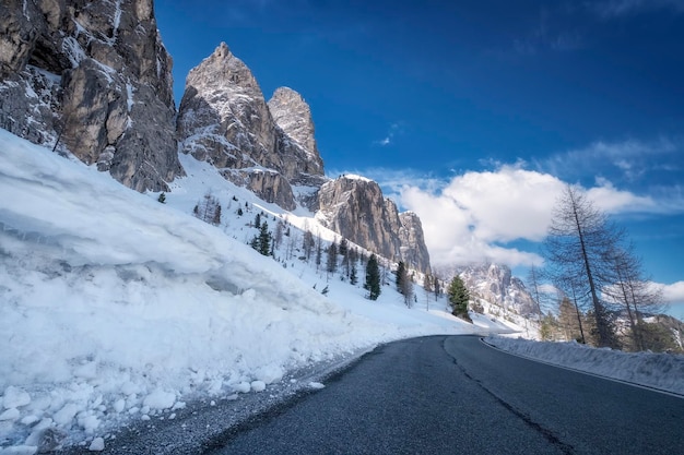 Scenic winter view from the asphalt road in the mountains covered with snow and trees on the side of the road on a background of blue sky and clouds South Tyrol North of Italy Gardena Pass