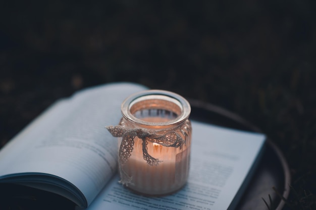 Scented burning candle stay on open paper book on wooden tray in dark Night time