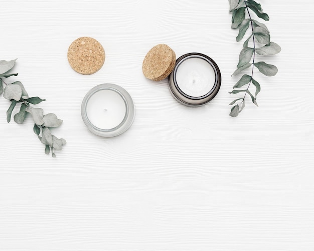 Scented candle in glass jar with natural ingredients on white wooden background with eucalyptus