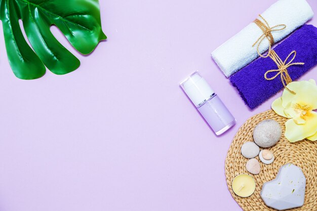 Scented candles, towel, lotion, pebbles and monstera leaf on a lilac background. Top view, copy space, flat lay. Spa and body care concept.