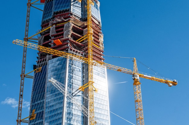 Schaal actief wolkenkrabbergebouw, schittering van de zon op de ramen, kranen tegen de blauwe hemel.