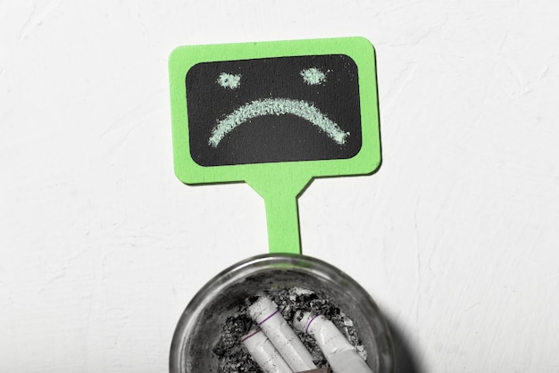 Schade aan roken concept Ongelukkige smiley en asbak met sigarettenpeuken Roken is een ongezonde en slechte gewoonte depressie door roken