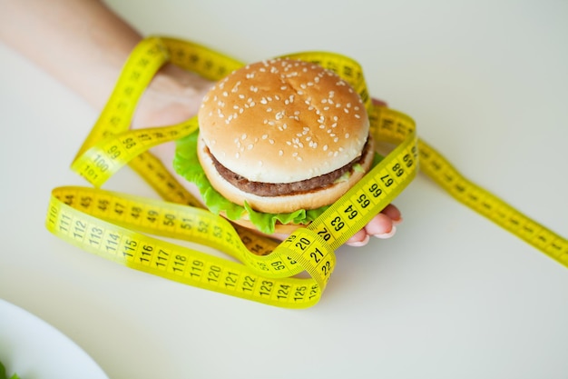 Schadelijk eten, dikke burger naast het gele meetlint.