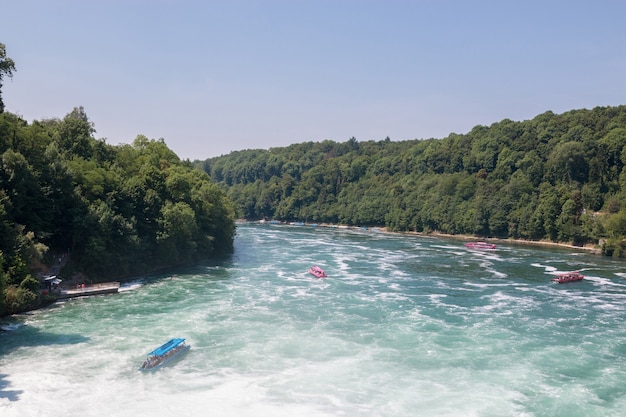 Schaffhausen, Switzerland - June 22, 2017: Boat with people floating to the waterfall the Rhine Falls. It is one of the main tourist attractions. Summer day with blue sky