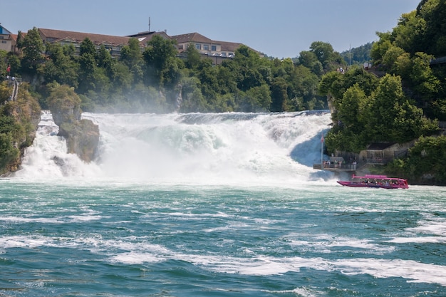 Schaffhausen, Zwitserland - 22 juni 2017: Boot met mensen drijvend naar de waterval de Rijn Falls. Het is een van de belangrijkste toeristische attracties. Zomerdag met blauwe lucht